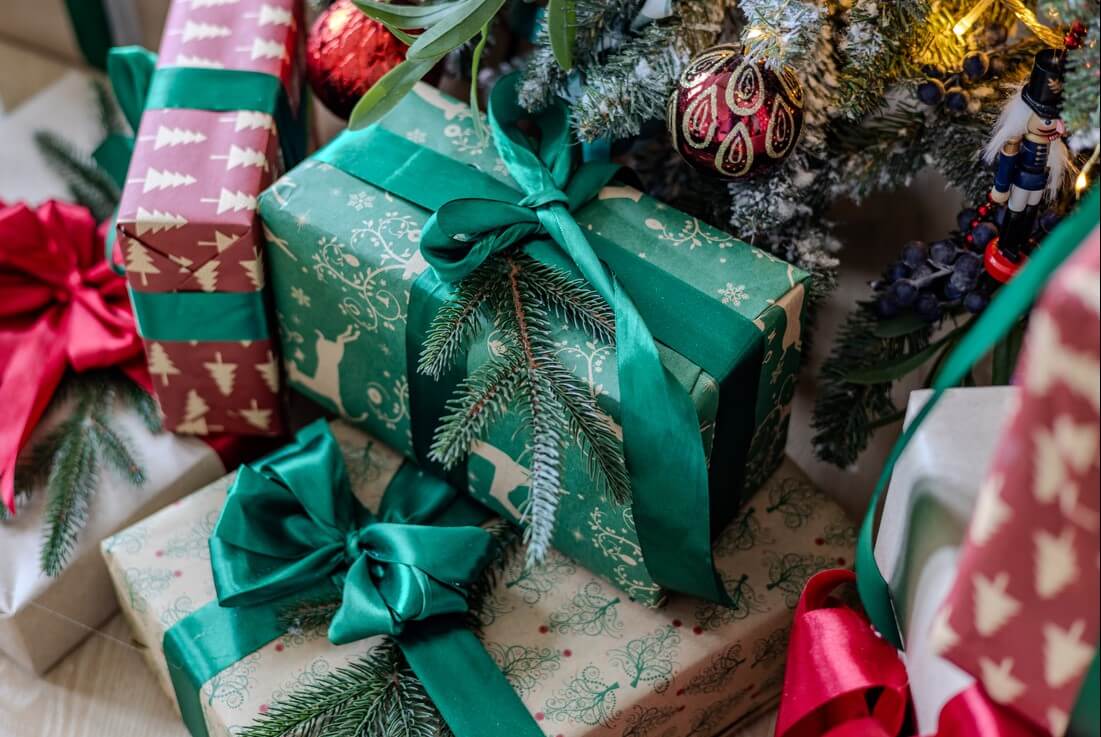 Wrapped gifts on the floor under a tree.