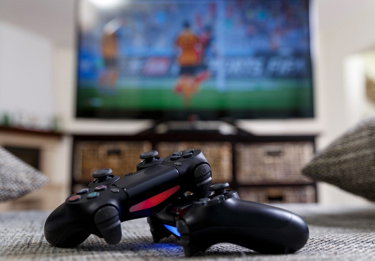 Two console controllers in front of a soccer game on the television.