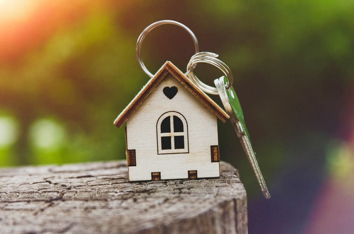 Closeup of a wooden house keychain sitting on a log.