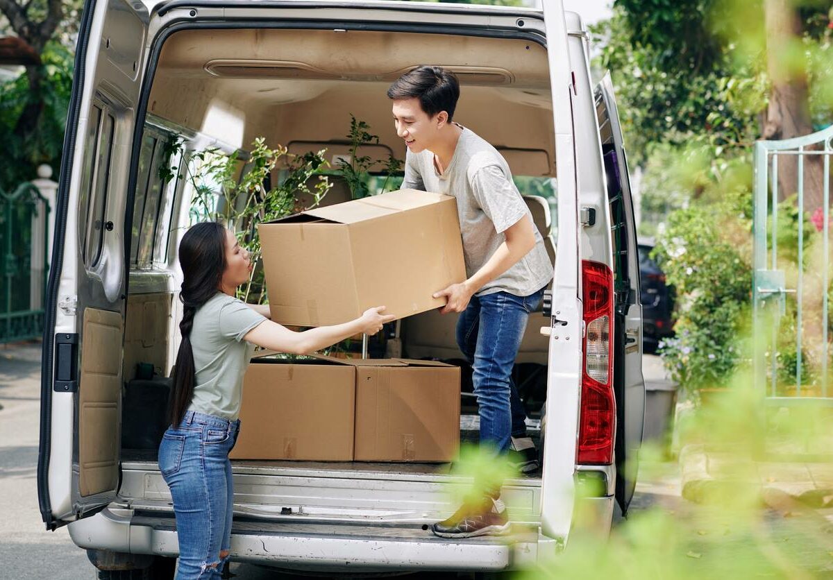 A couple unloads a moving truck together during the day.