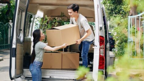 A couple unloads a moving truck together during the day.