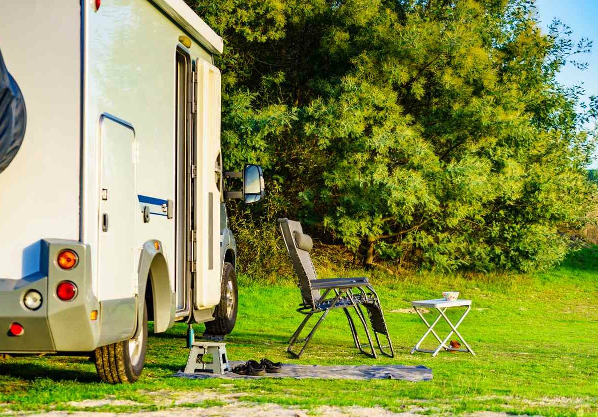 An RV campsite on a green natural area with a lawn chair and table set up.
