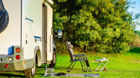 An RV campsite on a green natural area with a lawn chair and table set up.