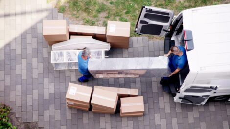 Two movers carry a large piece of furniture into a moving van.